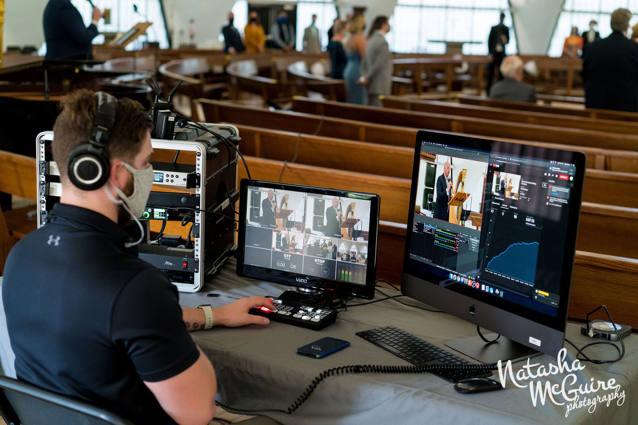 A Metrospect Media employee in a black polo sits at the back of a church surrounded by high-tech video equipment. On the screens in front of him are videos showing a live streaming event currently being captured.