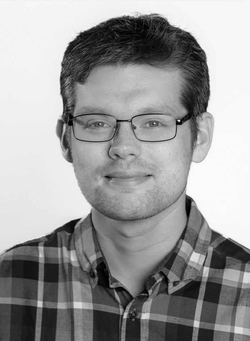 Black and white headshot of co-owner Molly. She is wearing a white shirt with a patterned blazer and is standing against a textured wall. 